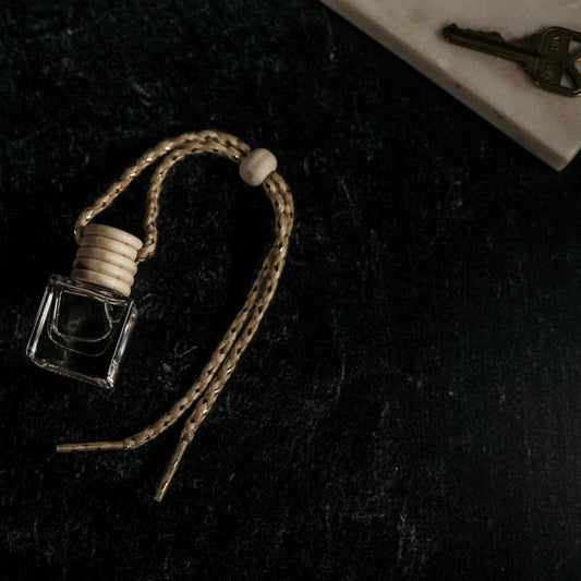 Natural car scent diffuser bottle with wooden cap and hanging braid on black surface